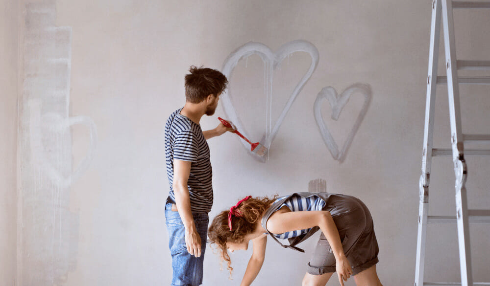 Mann und Frau sind dabei Sumpfkalkfarbe zu verarbeiten. Sie malen Herzen auf eine Wand